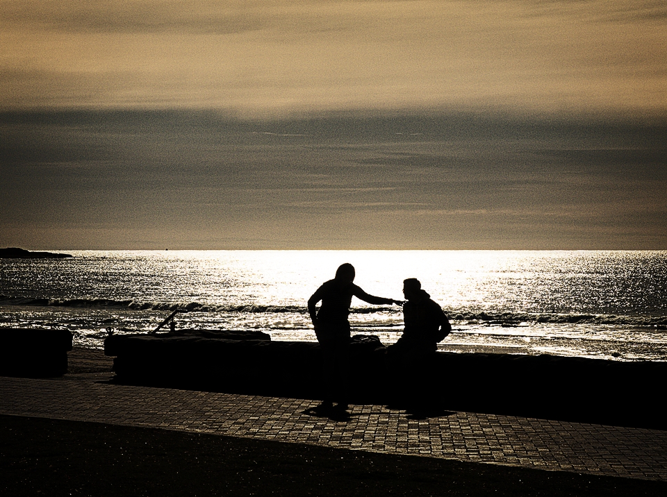Silhouette beach scene, one person touches the other on the shoulder.